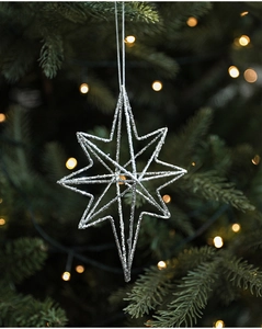 Silver glitter star ornament hanging on green pine branch with warm bokeh lighting