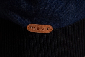 Makroaufnahme der Strickstruktur und des Marken-Lederlogos mit Metallnieten am Ärmel