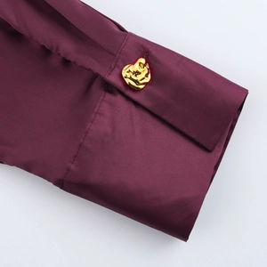 Detailed close-up of dark purple silk blouse cuff featuring a unique gold metal button