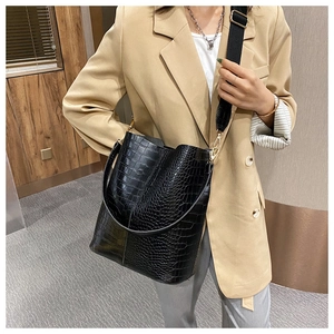 Detailed shot of black crocodile embossed bucket bag with wide nylon strap and gold hardware