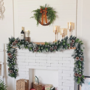 Detail of snowy flocked Christmas garland with pine cones and red bow on white fireplace