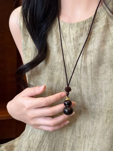 Detail of wooden gourd pendant on black woven rope necklace over a green garment