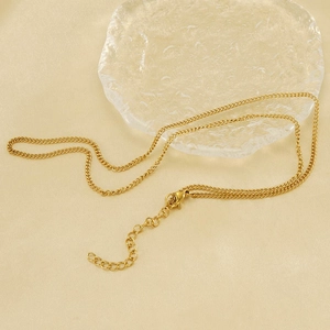 Nahaufnahme der goldenen Edelstahl-Weizenkette mit Karabinerverschluss auf Seide und Glas