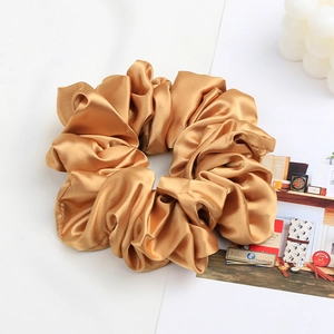 Detail of champagne gold satin scrunchie with elegant pleated fabric texture