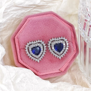 Detail of blue heart-shaped stud earrings with white zircon halo on a pink velvet box