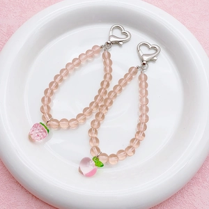 Pink transparent beaded phone straps with strawberry and peach pendants in ceramic dish