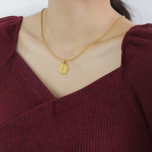 Close-up of gold 18K rope chain necklace with oval floral pendant on burgundy sweater
