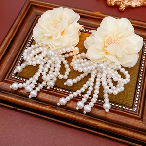 Close-up of cream camellia earrings featuring elegant white pearl tassels on a frame