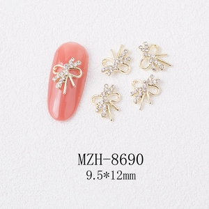 Detail of 9.5x12mm golden bow nail charms with white rhinestones on texture background