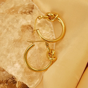 Elegant gold titanium steel knot hoop earrings on shimmering silk and crystal background