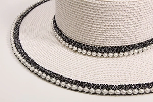 Detailed close-up of straw sun hat with black woven band and elegant pearl embellishments