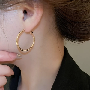 Close-up of model wearing large minimalist golden hoop earrings with polished metallic finish