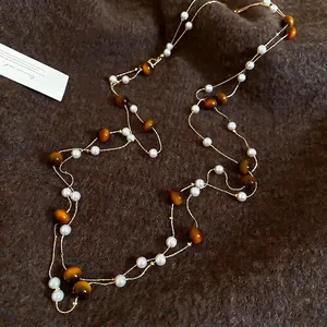 Elegante mehrlagige Tigerauge- und Perlen-Halskette auf braunem Strickhintergrund