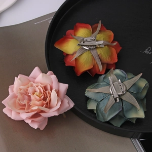 Three elegant fabric flower hair clips in pink and orange gradients on a desktop