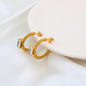 Elegant gold twisted C-shape earrings with rectangular zircon on white silk background