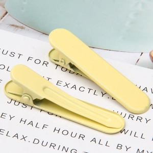 Detail of two matte yellow metal hair clips on a minimalist white card and blue background