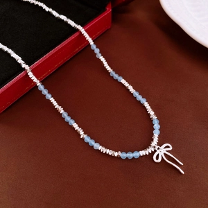 Detail of silver beaded necklace with light blue crystal beads and bow pendant