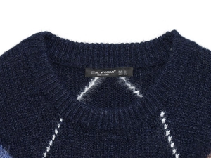 Close-up of crew neck navy knit sweater with white geometric pattern and brand label