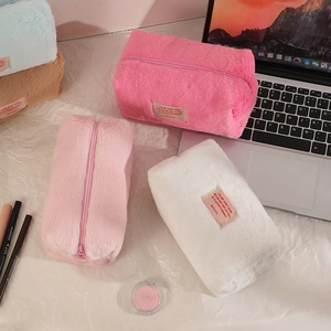 Solid color plush makeup bags in pink, white, blue and brown arranged on a desk