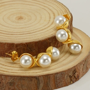Gold stainless steel S-shaped earrings with three round pearls on wood background