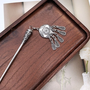 Detailed view of ancient style silver hair stick with tassel on a dark wooden tray