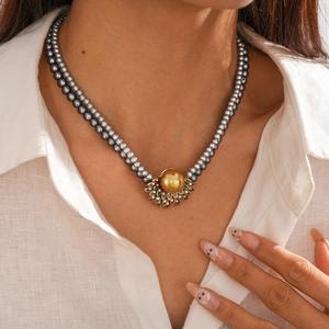 Dettaglio collana a doppio giro di perle grigie con ciondolo in oro e strass sul collo