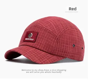 Detailed close-up of red plaid five-panel baseball cap with leather brand patch and eyelets