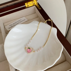 Dettaglio del ciondolo a cuore di pesca e perle su bracciale a catena d'oro regolabile