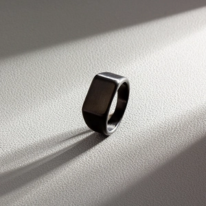 Detail of matte black rectangular signet ring with brushed finish on textured background