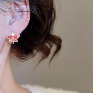 Detailed close-up of a golden maple leaf earring with red crystals on an earlobe