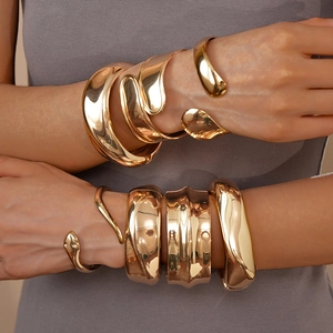 Dettaglio di bracciali ovali dorati impilati con finiture metalliche lucide e brillanti