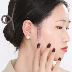 Close-up of golden pearl earring and brown minimalist hair claw on female model