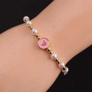 Close-up of beaded bracelet with pearls, gold beads and pink heart enamel charm