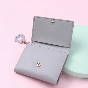 Detail of grey pebble leather cat claw charm and snap closure on a compact trifold wallet