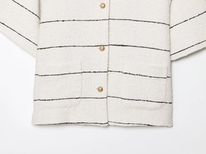 Dettaglio giacca in tweed a righe bianche con bottoni dorati e trama intrecciata