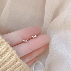 Close-up of minimalist silver X-shaped earrings held on fingertips with soft background