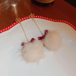 Detail view of winter Christmas earrings with white pompom and red bow on a ceramic plate