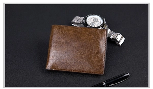 Brown leather bi-fold wallet for men styled with a metallic watch and pen on dark wood