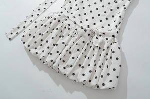 Détail d'une robe courte blanche à pois avec nœud à la taille et ourlet plissé