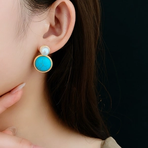 Close-up of vintage earrings with white pearl and turquoise stone on golden metal base