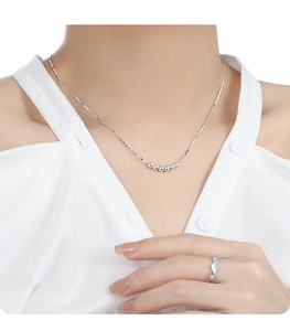 Gros plan d'un collier chaîne à perles argentées et bague géométrique sur un mannequin