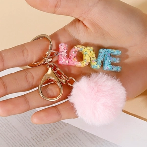 Detail of LOVE resin keychain with glitter stars and soft pink pompom held in hand