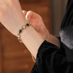 Détail d'un bracelet vintage doré avec pierres noires ovales et strass sur un poignet
