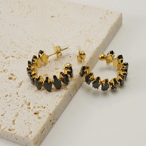 Detalle de pendientes de oro de 18K con circonitas negras sobre piedra beige
