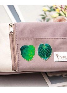 Macro detail of tropical leaf enamel pins pinned on a purple fabric pencil case