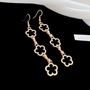 Detail of gold clover drop earrings with three hollow flowers on white silk background