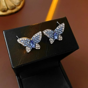 Primer plano de pendientes de mariposa con cristales azules sobre estuche de cuero
