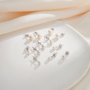 Collection of round white freshwater pearl earrings on a white ceramic tray and silk