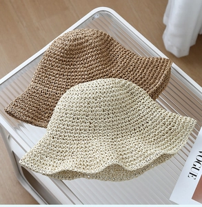 Detail of woven straw bucket hats in beige and caramel on a glass table surface