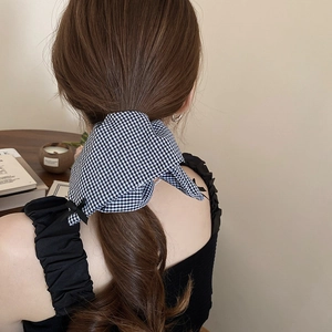 Detail of a black and white checkered bow hair tie worn on hair in a cozy setting